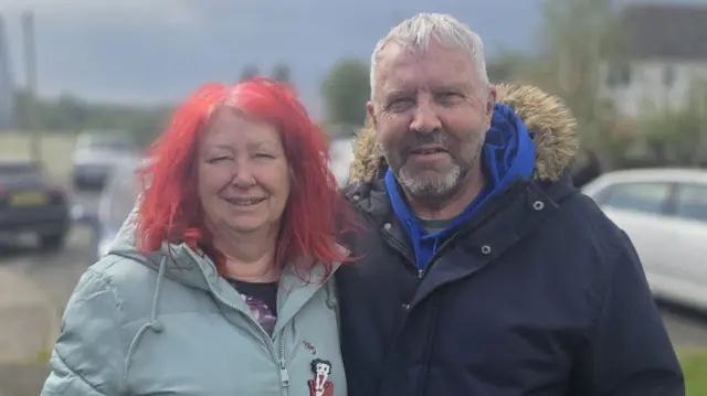 Bob and Joyce hugging in front of the community centre.