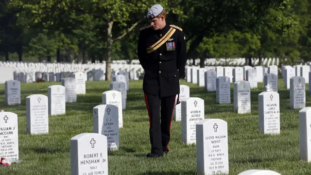 Prince Harry, wearing a military uniform, walking through rows of gravestones