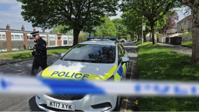 A police cordon with a police officer and a car in the background.