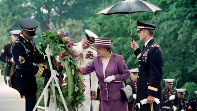 Queen Elizabeth II, wearing all purple, laying a wreath at tomb, surrounded by soldiers