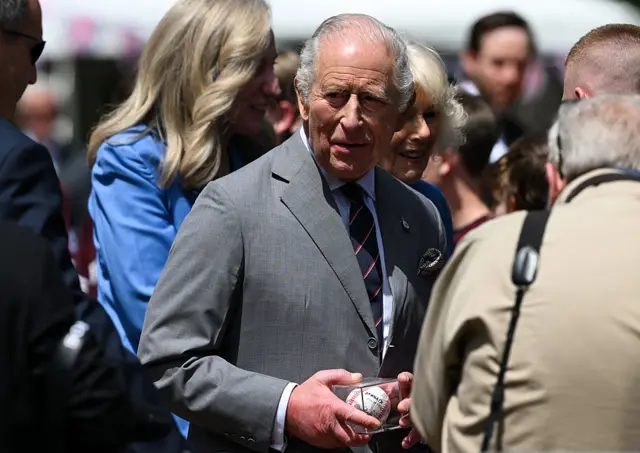 King Charles holds a baseball in a glass case as he and the Queen greet crowds