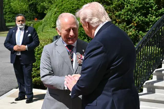 The King and president shake hands while smiling on a bright sunny day