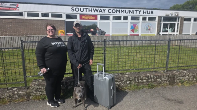 Natasha and Scott stood with their dog and suitcase.