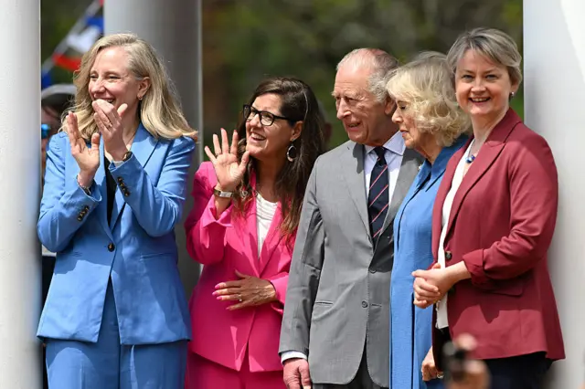 King, Queen and other officials wave to crowds as they watch a marching band perform