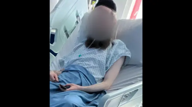 A bearded man in a hospital bed with his face blurred.