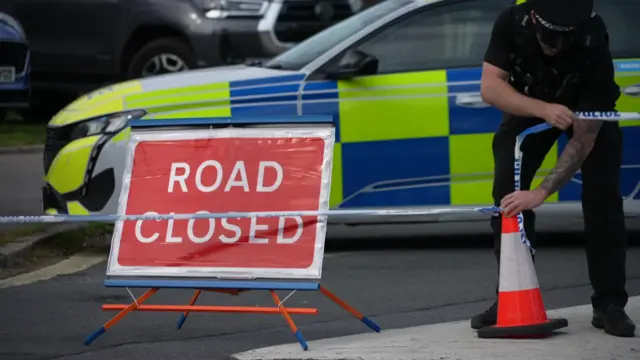 A police cordon with a road closed sign.