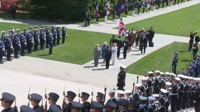 king and queen standing surrounded by honour guard