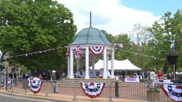 a gazebo decorated with British and American flags, with a tent in the distance and people standing around