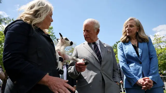 King Charles holds the hoof of a lamb, which is in the arms of its keeper