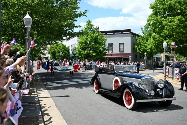 A vintage car drives down main street in a small town as part of a parade