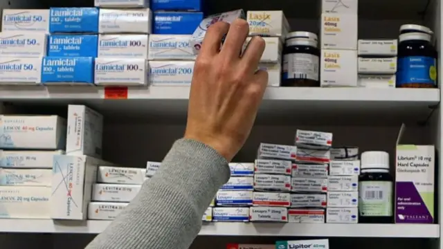 A hand reaches out to medicines at a pharmacy.