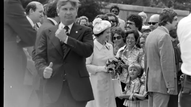 Queen Elizabeth II smiling and greeting onlookers at the cemetery