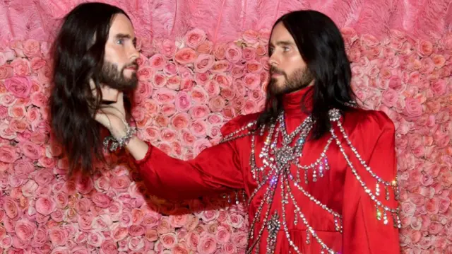 Jared Leto poses on the red carpet holding a bust of his own head