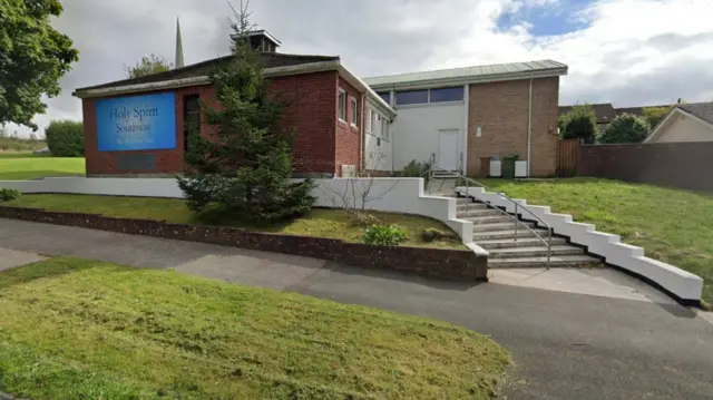 A modern single storey church with a tree and grass around it.