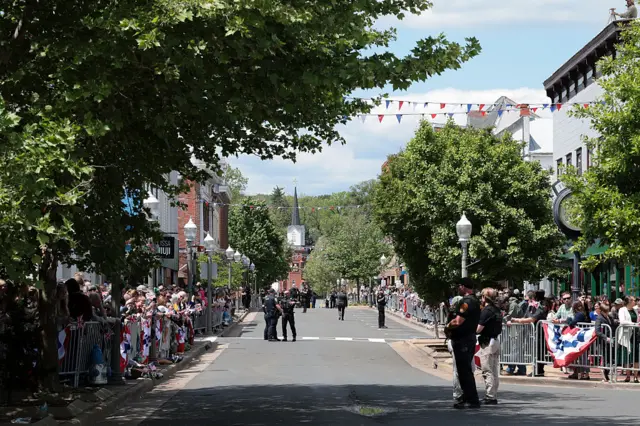 A small town American street lined with crowds awaiting the King and Queen