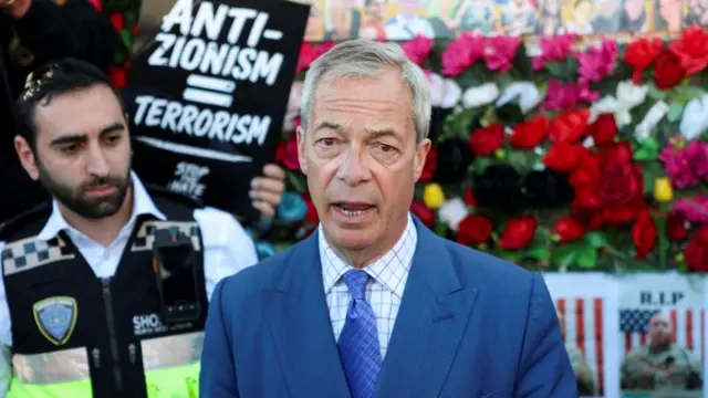 Nigel Farage stands in front of flowers wearing a blue suit, striped shirt and purple tie