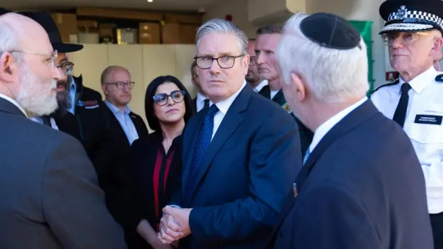 Starmer, standing next to Shabana Mahmood and Mark Rowley look at a jewish man who speaks to them. Other men stand around them looking on