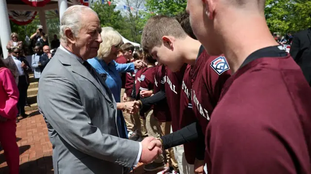 The king shakes hands with members of a youth baseball team dressed in red uniforms