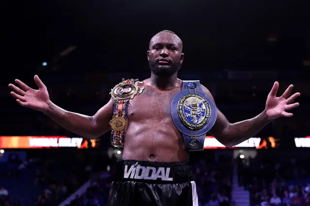 Viddal Riley holds out his arms and has the European and British cruiserweight titles over his shoulder