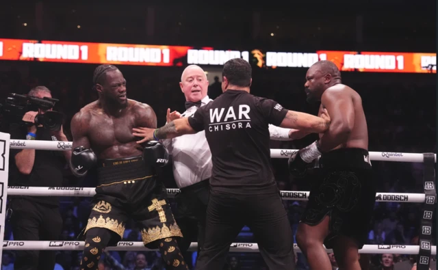 The referee and a cornerman stands in between Deontay Wilder and Derek Chisora