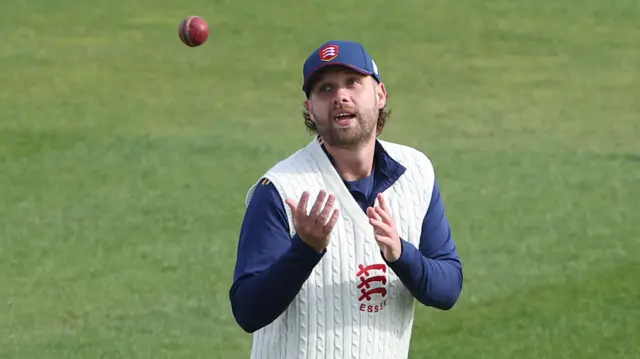 Matt Critchley in a sleeveless Essex jumper prepares to catch a ball