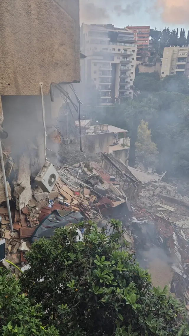 Smoke rises from the rubble of a partially collapsed building.