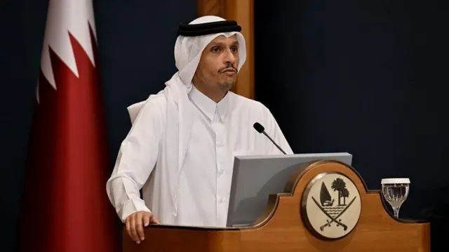Al-Thani, wearing all white, stands and speaks at a podium