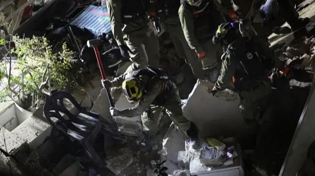 A man with a sledge hammer digs in rubble