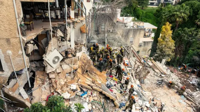 Emergency service workers stand in the rubble of a building in Haifa, Israel, after an Iranian strike.