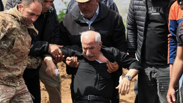 a sobbing man falling to his knees as other men hold him back