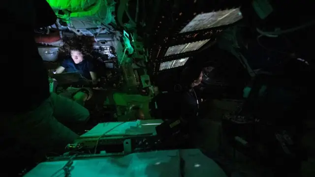 Nasa astronaut Christina Koch is illuminated by a screen she is looking at inside the darkened Orion spacecraft, with some green lights illuminating the walls