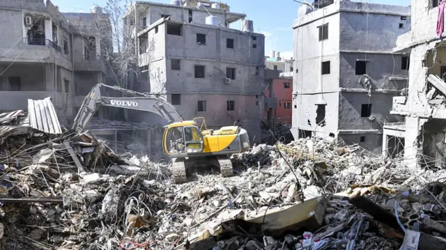 an excavator standing on top of a massive mound of rubble of a destroyed building