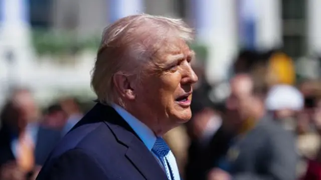A side view of Donald Trump outside with a crowd in the background.