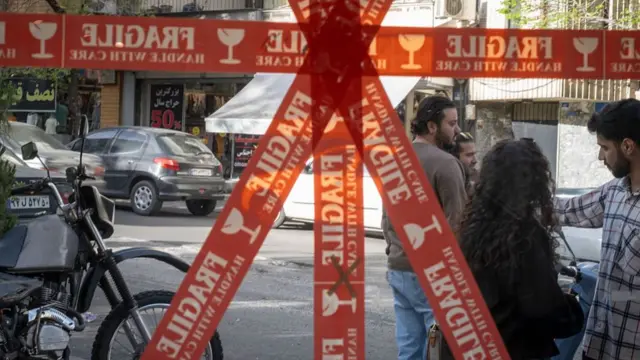 Iranians outside a cafe in Tehran on Sunday, as tape covers the windows to protect them from shattering