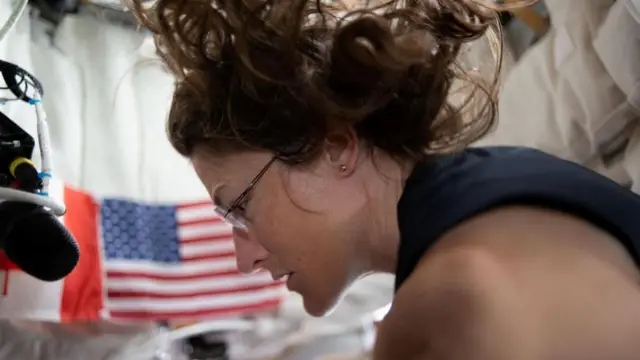 Nasa astronaut Christina Koch in a side-profile picture with an American flag blurry in the background and her curly brown hair floating due to lack of gravity
