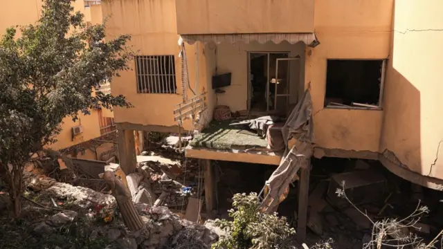 The bottom floor of a building has been turned to rubble. A damaged balcony can be seen above it