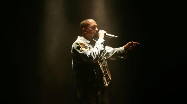Kanye West raps under a spotlight on stage at Glastonbury