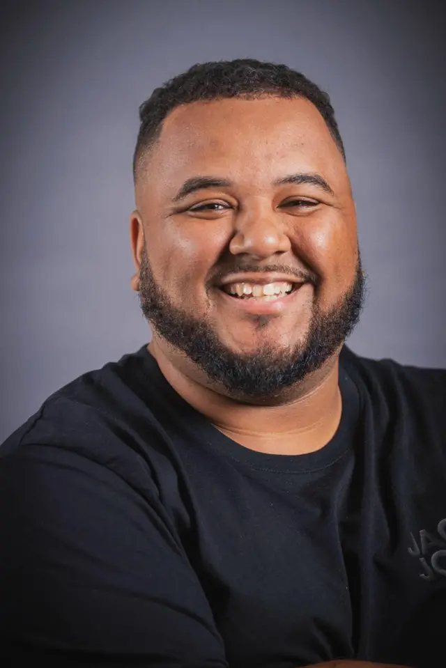 Otis Haughton smiles with his arms folded in a head shot photo