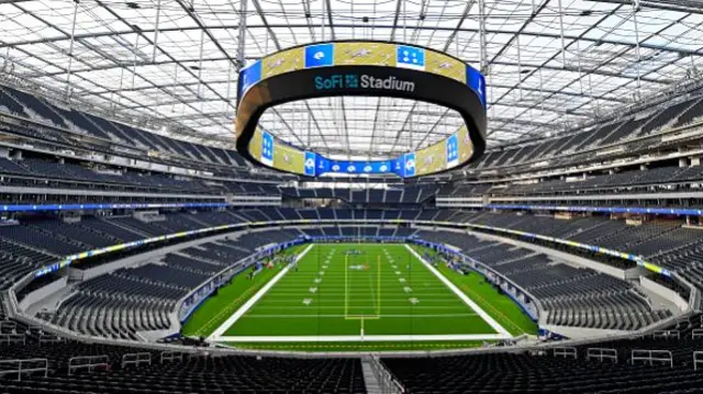 The empty stands of the SoFi stadium can be seen from the edge of the stand. A large circular screen sits above the pitch