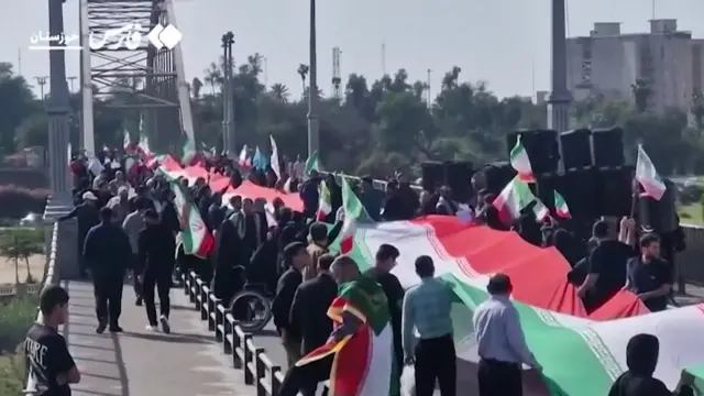 Iranians gather on a bridge holding a large flag