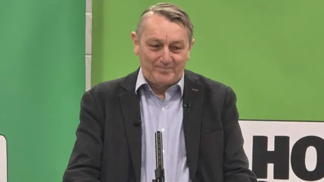 Anthony standing on a podium wearing a navy suit.