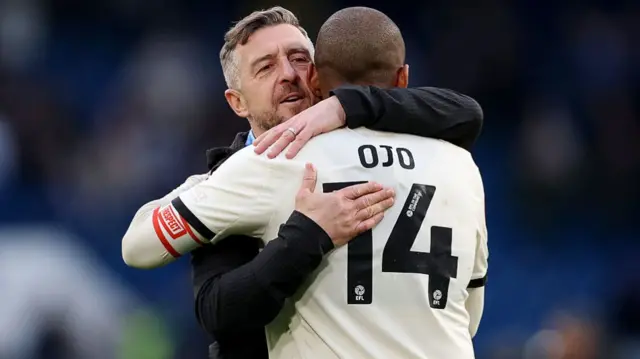 Jon Brady, manager of Port Vale, and Funso Ojo embrace after the FA Cup Quarter Final match between Chelsea and Port Vale
