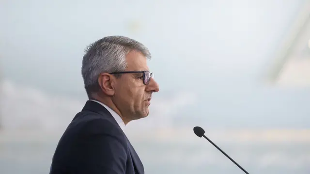 Iran foreign ministry spokesperson Esmaeil Baqaei speaking into a microphone from a side profile and looking towards the right side of the frame, with a blurry light background behind him