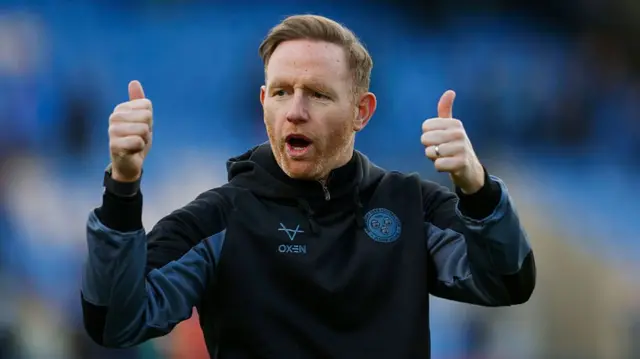 Shrewsbury boss Gavin Cowan gives both thumbs up to supporters while wearing a blue club tracksuit