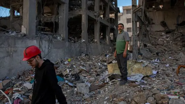 Two men stand among rubble of a blown out building