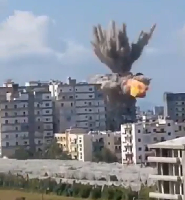 A screengrab showing he moment of an explosion on the top of a high-rise building and a large smoke cloud being thrown up, there are several other apartment blocks nearby.