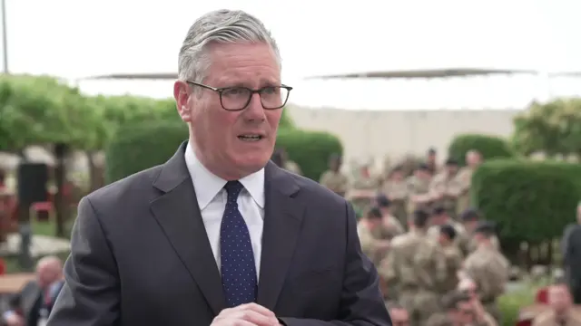 Keir Starmer on the left of the frame speaking towards the right with blurred trooops in the background