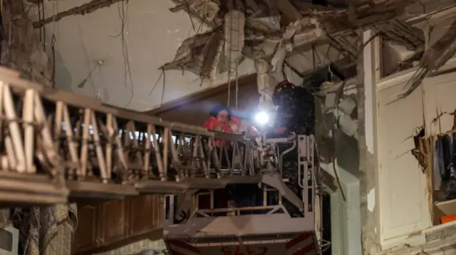 A rescuer extended from a ladder helps a woman who is trapped in rubble