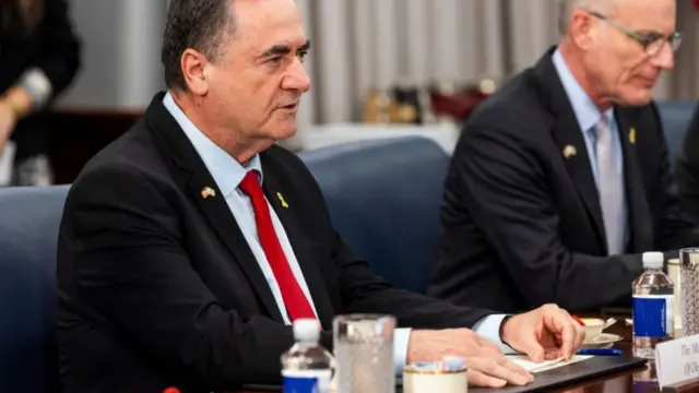 Israel Katz sits at a table during a meeting, wearing a dark suit, light-coloured suit and red tie.