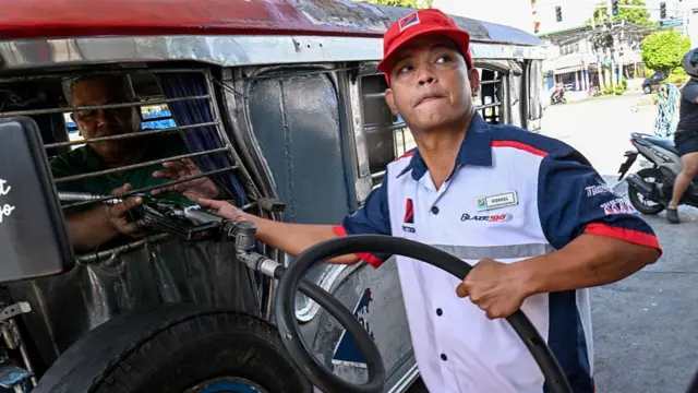 A petrol station attendant helps a customer top up his vehicle while keeping an eye on the pricing meter